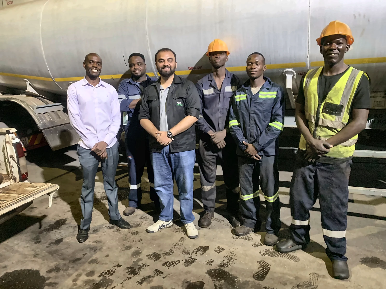 Six people, most in work overalls and hard hats, in front of a fuel tanker at a depot in Harare