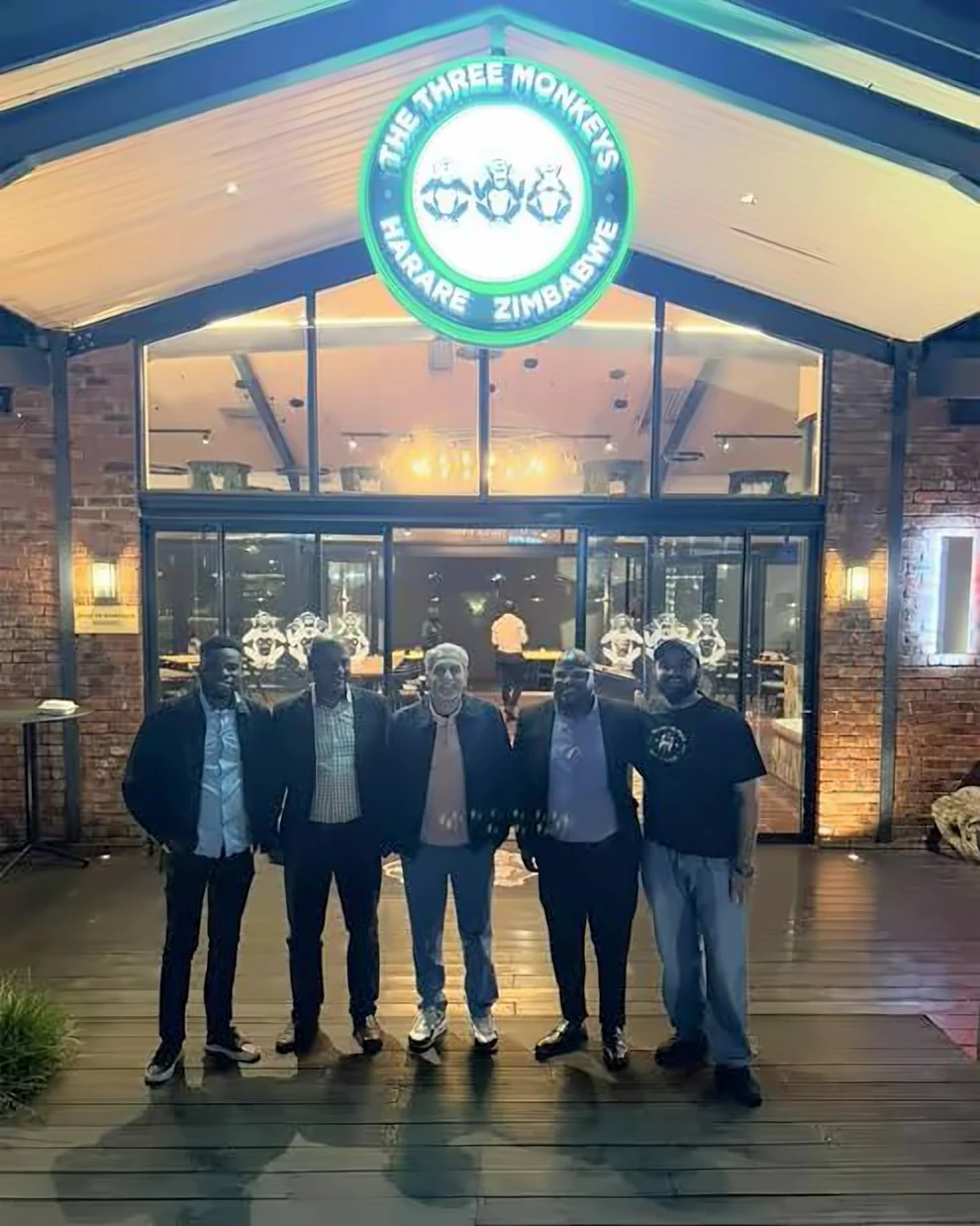 Five members of the team standing outside The Three Monkeys restaurant in Harare at night